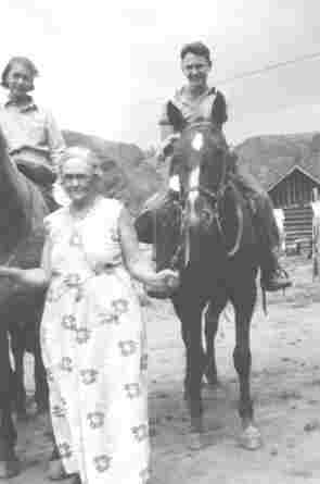 A black and white photo of two teenagers on horses with an older woman in a white dress with large flowers holding their reins in Almont, Colorado in the 1930's.