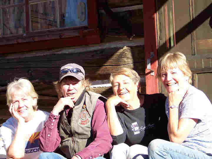 Polly and three sisters in front of an old log cabin, each with her chin on her right hand and elbows on knees.