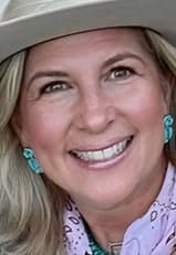 Lisa Youngblood smiling with a pink scarf, turquoise earrings, and a beige cowboy hat.