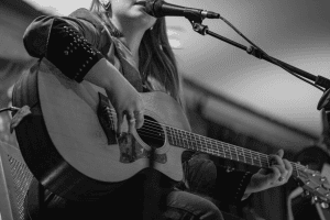 SJ McDonald singing and playing guitar in black and white.