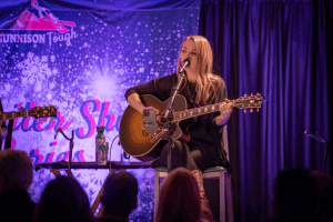 Autumn McEntire singing on a stage with purple and pink Gunnison Tough banners and curtains.
