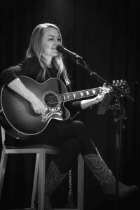 Autumn McEntire singing with soft lighting on her hair and guitar in black and white.