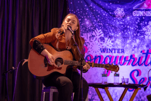 SJ McDonald singing with her eyes closed and playing a guitar.