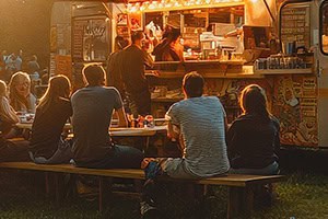 Hungry customers sit at picnic tables and eat terrific food from a food truck.