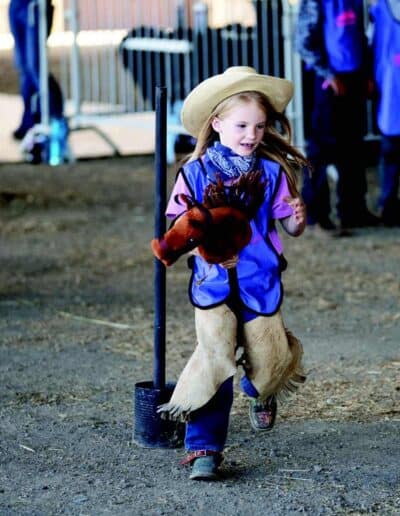 A girl with cowboy hats competes on a stick horse in the Bull Fest barnyard olympics.