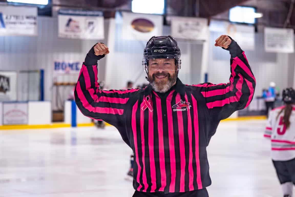 Pink in the Rink 2026 Ref showing his muscles in a pink and black striped shirt.
