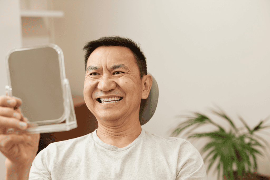 Man smiling while examining a mirror, considering dentures.