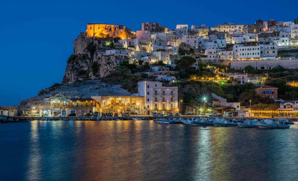 View of the town of Peschici from the sea at dusk with the lights of the town reflecting on the sea