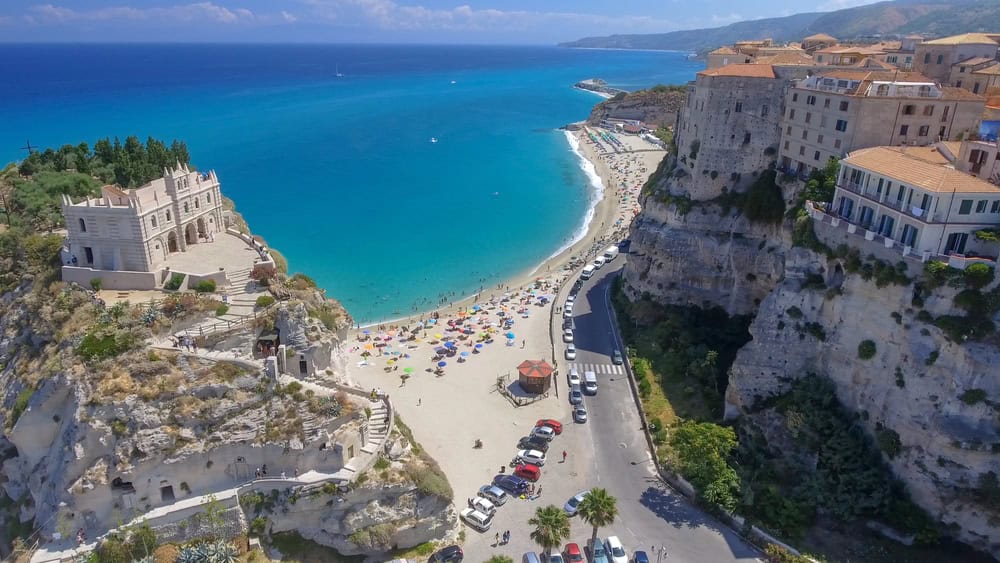 Aerial view of church Santa Maria Dell'Isola and old town buildings of tropea on cliff top, with white sand beach and turquoise sea, for post 'things to see in Tropea'.