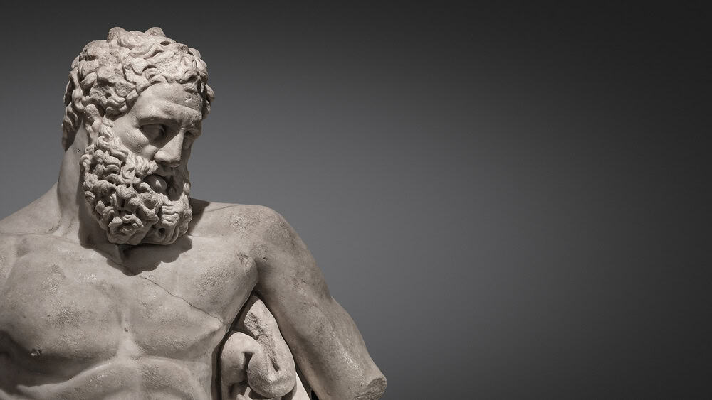 Marble Stone sculpture of a bearded man Hercules showing his upper torso with a graded grey background.