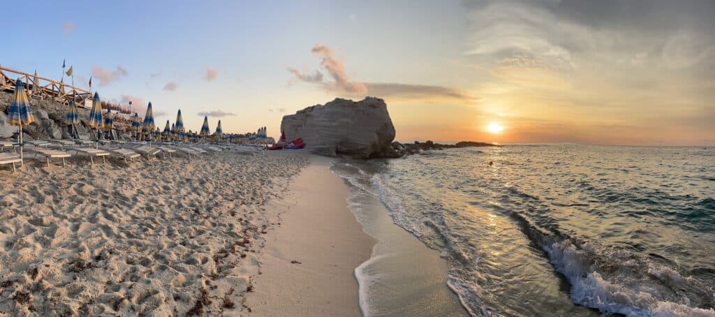 Scenic view of Tropea beach at sunset with large rock formation and calm sea.