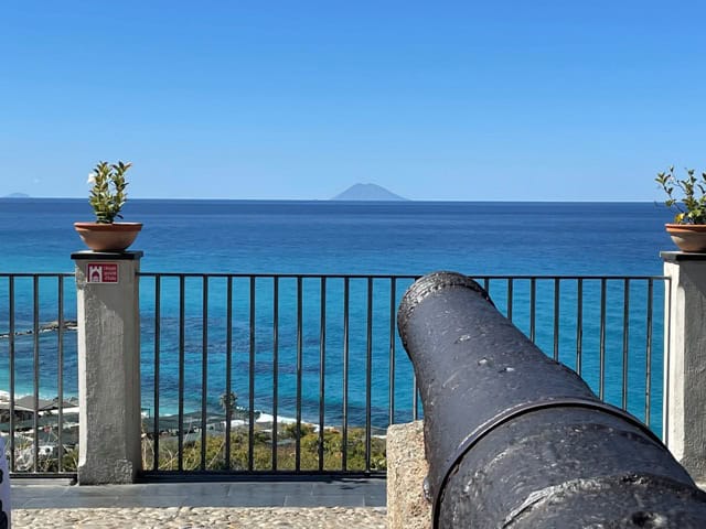 view from a square with old steel cannon aiming towards the blue sea and the isalnd of Stromboli a cone shaped island on the horizon, on a cloudless sunny day.