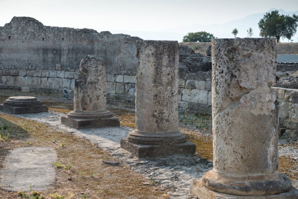 image of remains of ancient stone roman columns with ancient stone walls in the background