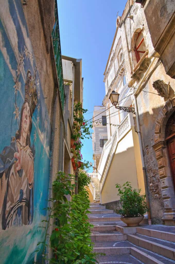 an narrow quaint alleyway with stone steps and a colourful mural with some green plants growing near the walls on a sunny day