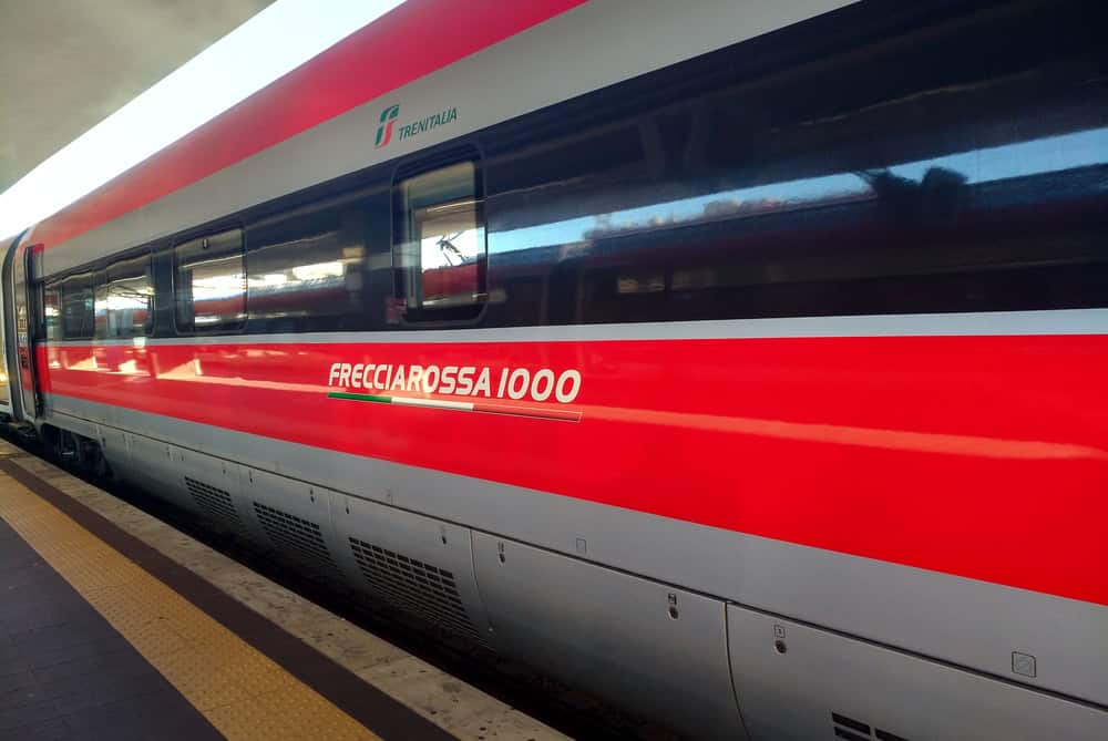 red and silver striped modern train stopped at the platform of a station