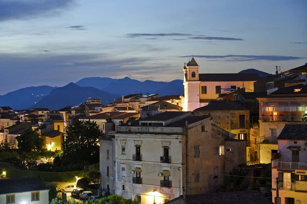 view at dusk with lights of the church and houses already on of a hilltop village with silhouettes of the mountains on the distant mountains on the horizon.