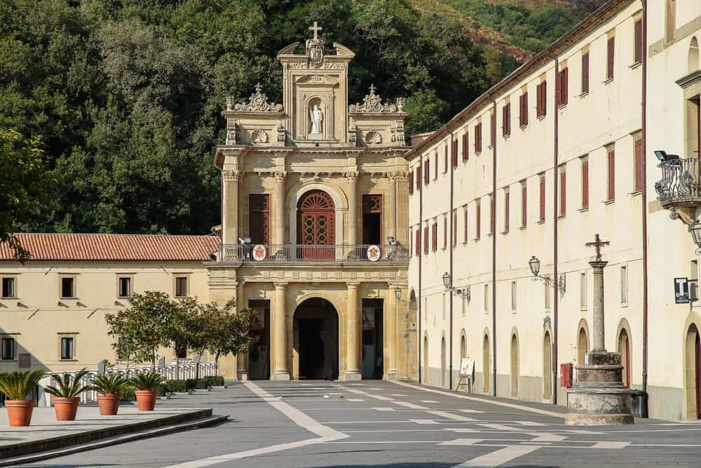 Facade and forecourt of a catholic stone church nestled in mountainous green landscape of dense trees of the sanctaury of Saint Francesco of Paola in calabria