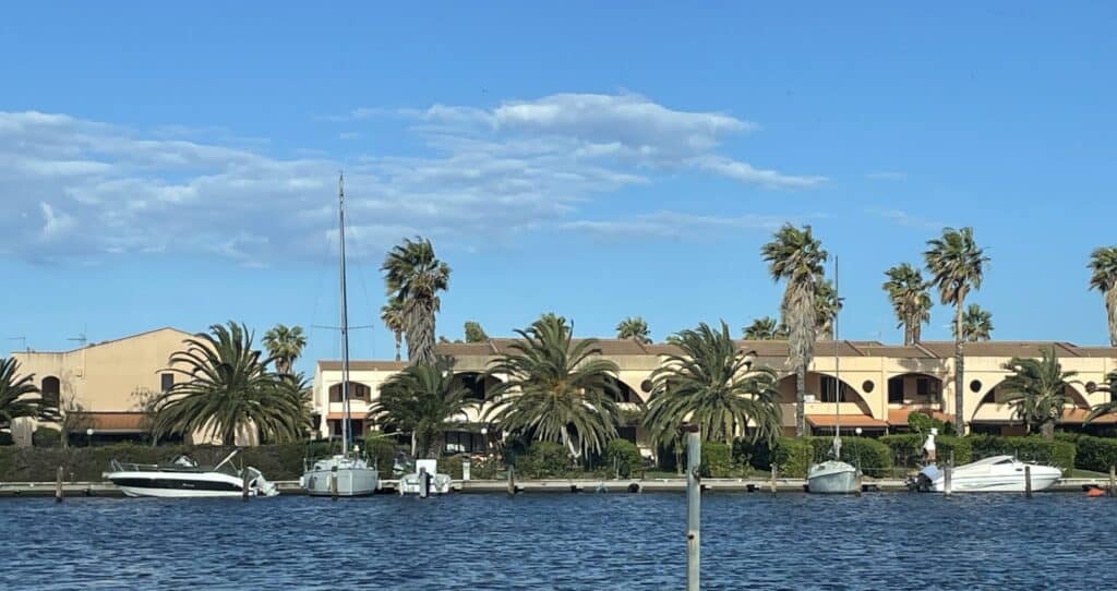 view of the water front on the lakes of Sibari and residences with palm trees and sailing boats moored alongside on a sunny day