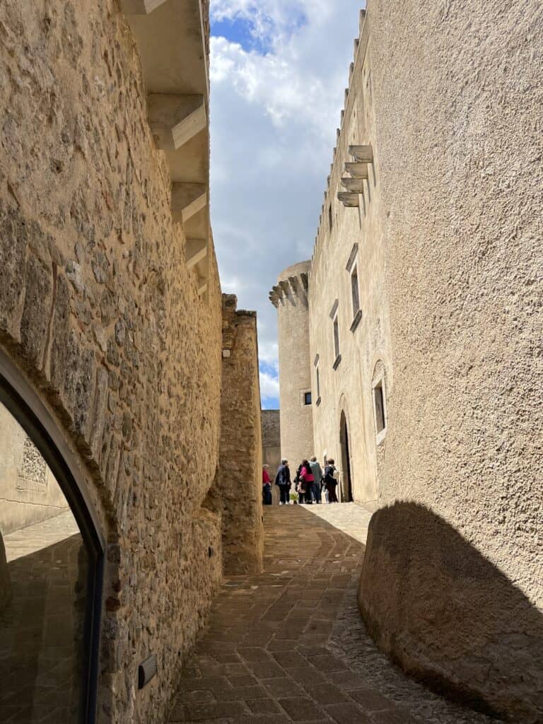 Image of a stone alleyway with high castle walls on a sunny day and a few people in the distance