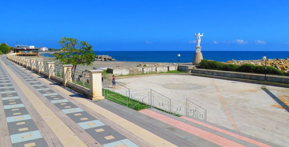 view of the seafront promenade with a statue of Christ facing the blue sea on a sunny day. 