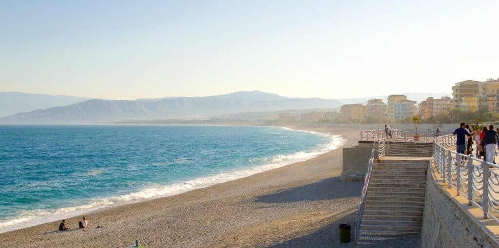 image of deserted long sandy beach  with blue sea on a sunny day with the buildings of the promenade on the land side and some people strolling on the promenade