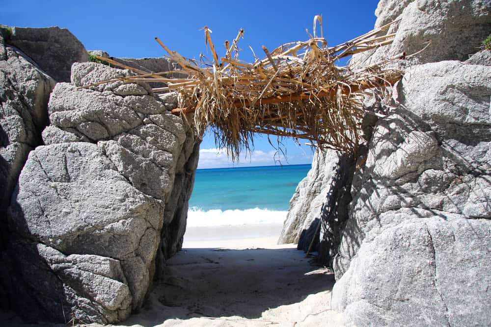 rocky outcrop , gap leading to white sand beach and blue sea, with rustic thatched roof over the gap and shade below