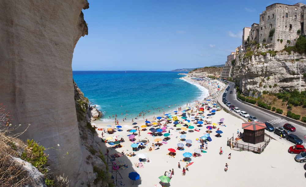 white sand beach and turquoise coloured sea with people and colourful beach umbrellas on a bright sunny day