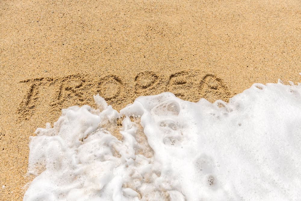 close up of the word Tropea written in the sand on a beach and a wave about to cover it