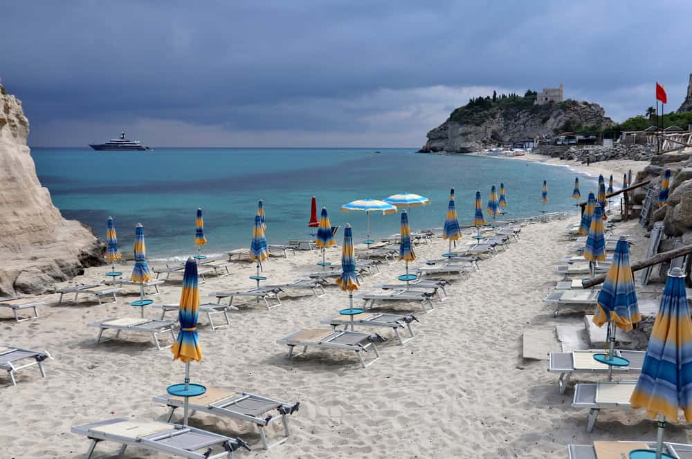 White sand beach and clear blue sea on a sunny day, with closed beach umbellas and beach loungers
