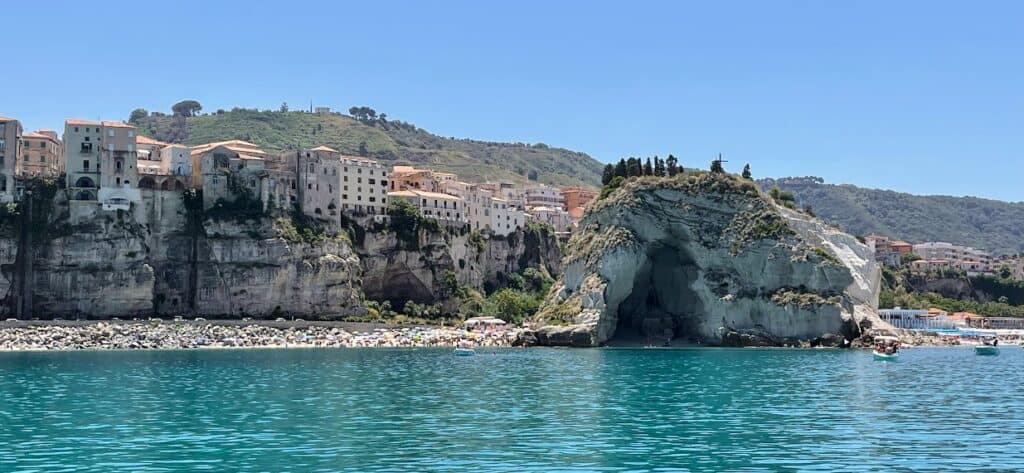 Scenic view of Tropea's coastline with cliffs and sea cave under a clear blue sky.