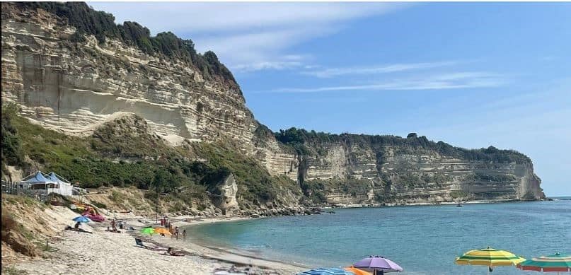 secluded white sand beach with few people.dramatic white cliffs on the edge of the beach and a clear blue sea on a sunny day. green vegetation at cliff top