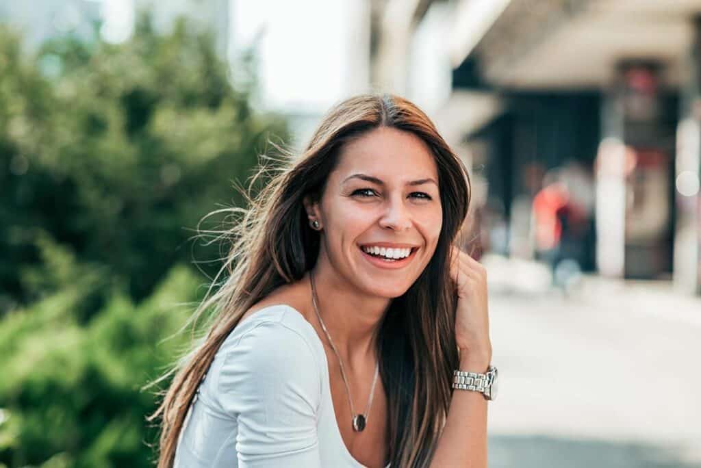 Bright smiling woman outside in urban setting, showcasing confident dental health, at Heritage Dental Centre Edmonton.