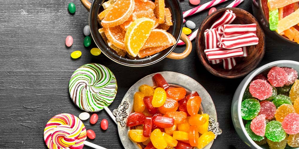 Colorful gummy candies and sweets on a dark wooden surface, featuring sugar-coated, fruit-flavored treats and lollipops.