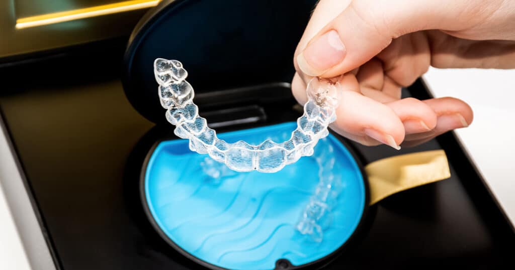 Clear dental aligner being sanitized in a blue UV sterilizer at Heritage Dental Centre, Edmonton's trusted dental clinic.