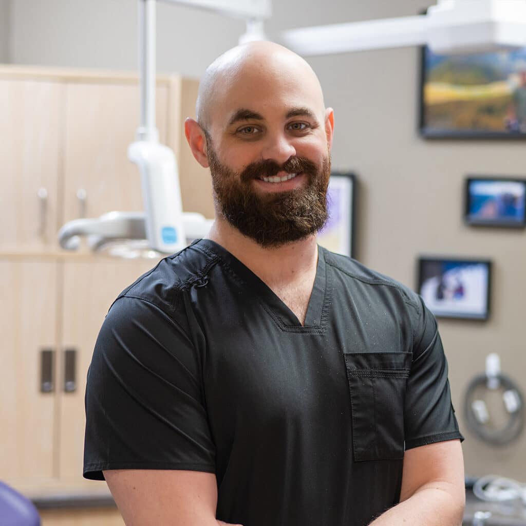 Friendly male dentist in black scrubs smiling at Heritage Dental Centre Edmonton dental clinic.