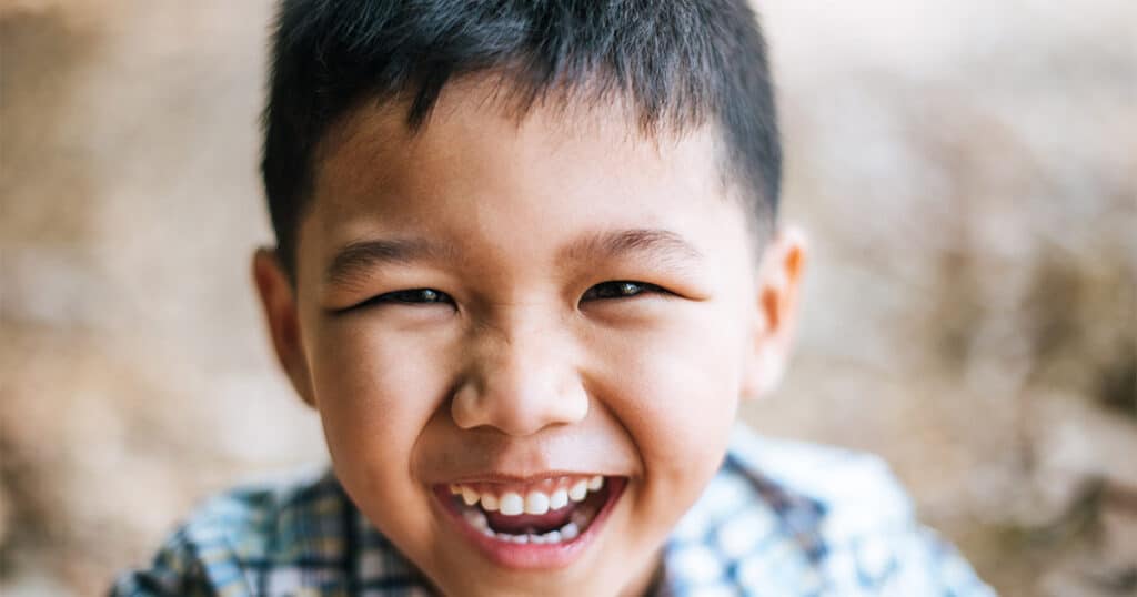 Bright smiling young boy showcasing healthy teeth, over blurred background.