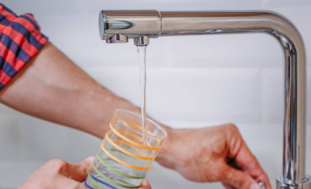 Clear water being poured into a colorful glass from a modern kitchen faucet at Heritage Dental Edmonton.