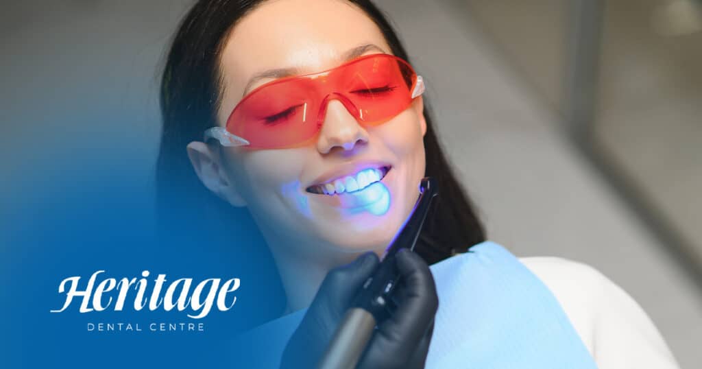 Porcelain teeth whitening procedure at Heritage Dental Centre in Edmonton, smiling woman with red protective glasses, modern dental treatment, cosmetic dentistry, patient comfort, professional dental care in Edmonton.