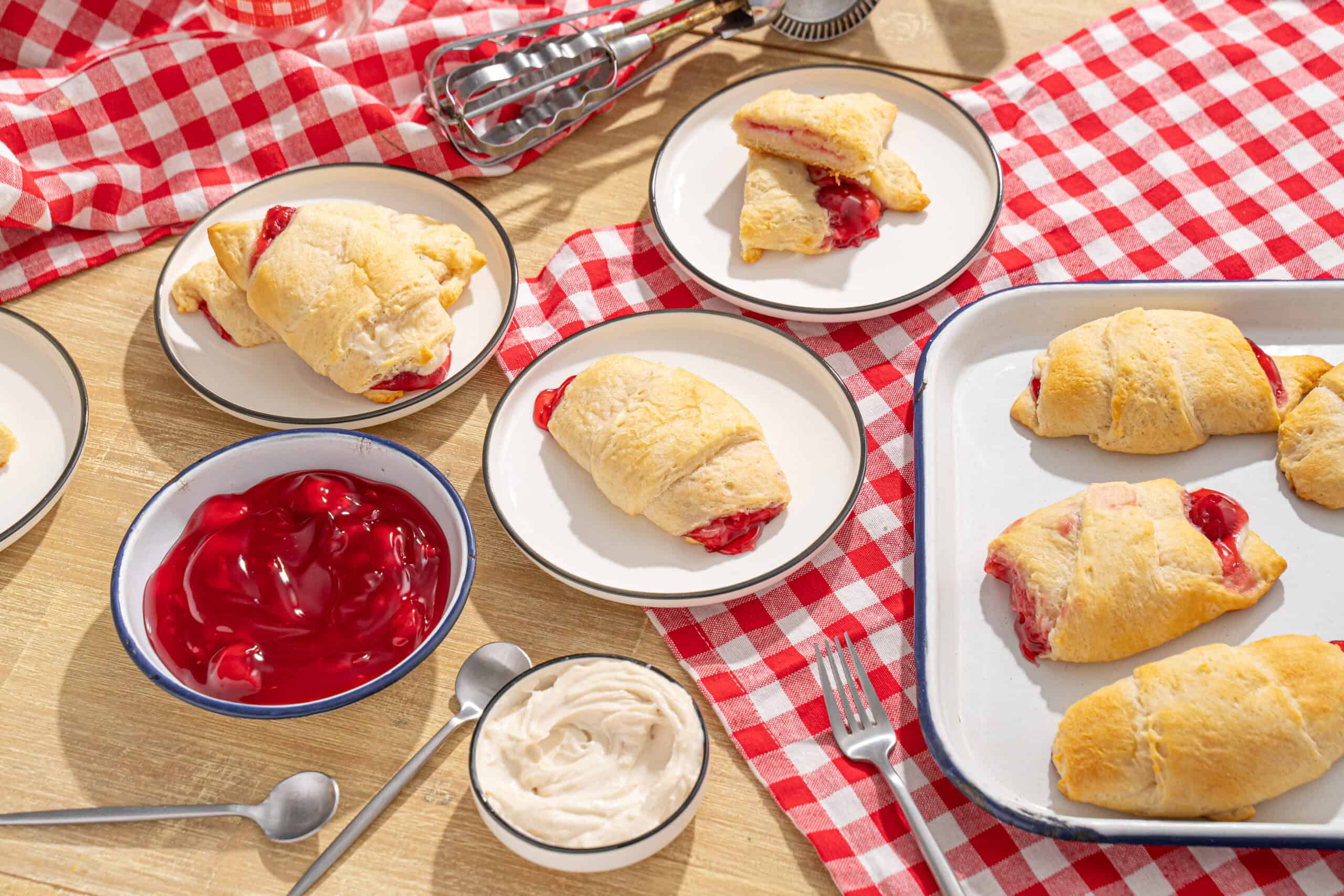 Flaky cherry-filled Danish pastries fresh out of the oven served on white plates on a wooden table with a red-checkered cloth.
