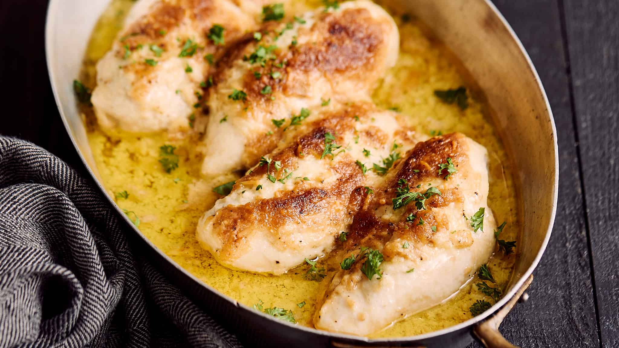Juicy baked chicken thighs in a creamy garlic butter sauce garnished with fresh parsley, served in a rustic skillet for a delicious and flavorful meal.