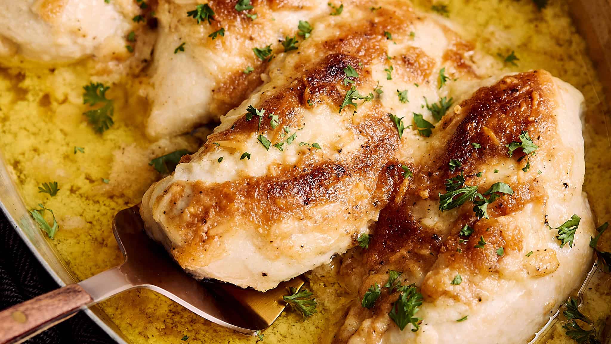 Juicy baked chicken thighs with golden crispy skin, garnished with fresh parsley, served in a flavorful yellow sauce in a baking dish.