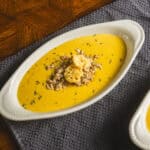 Creamy pumpkin soup with shredded chicken and croutons garnished with herbs, served in white oval bowls. Perfect for cozy fall dinners, this hearty soup recipe combines rich flavors and smooth texture.
