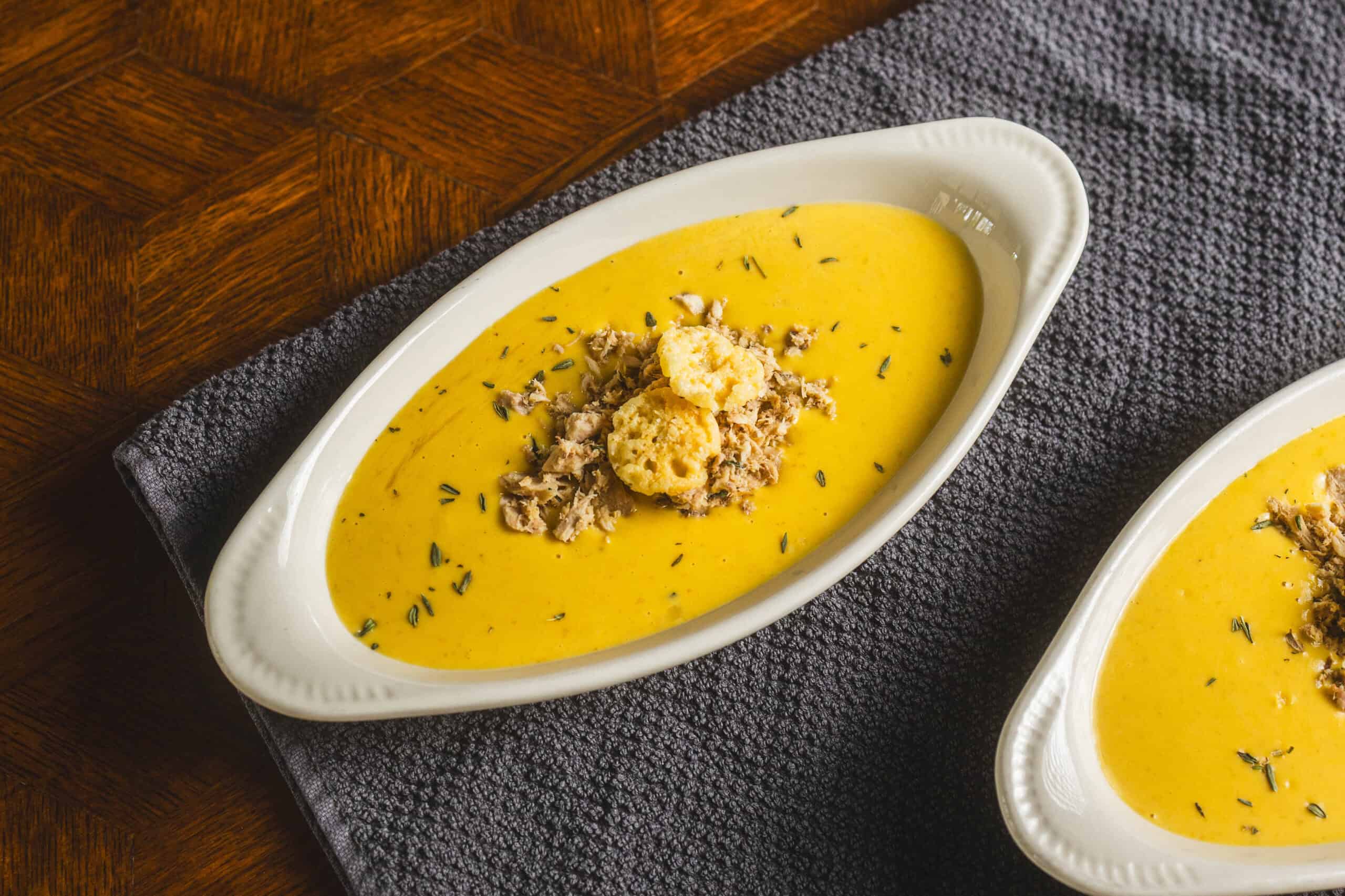 Creamy pumpkin soup with shredded chicken and croutons garnished with herbs, served in white oval bowls. Perfect for cozy fall dinners, this hearty soup recipe combines rich flavors and smooth texture.