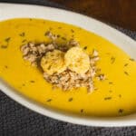 Creamy butternut squash soup garnished with shredded chicken and croutons in an oval bowl on textured placemat.