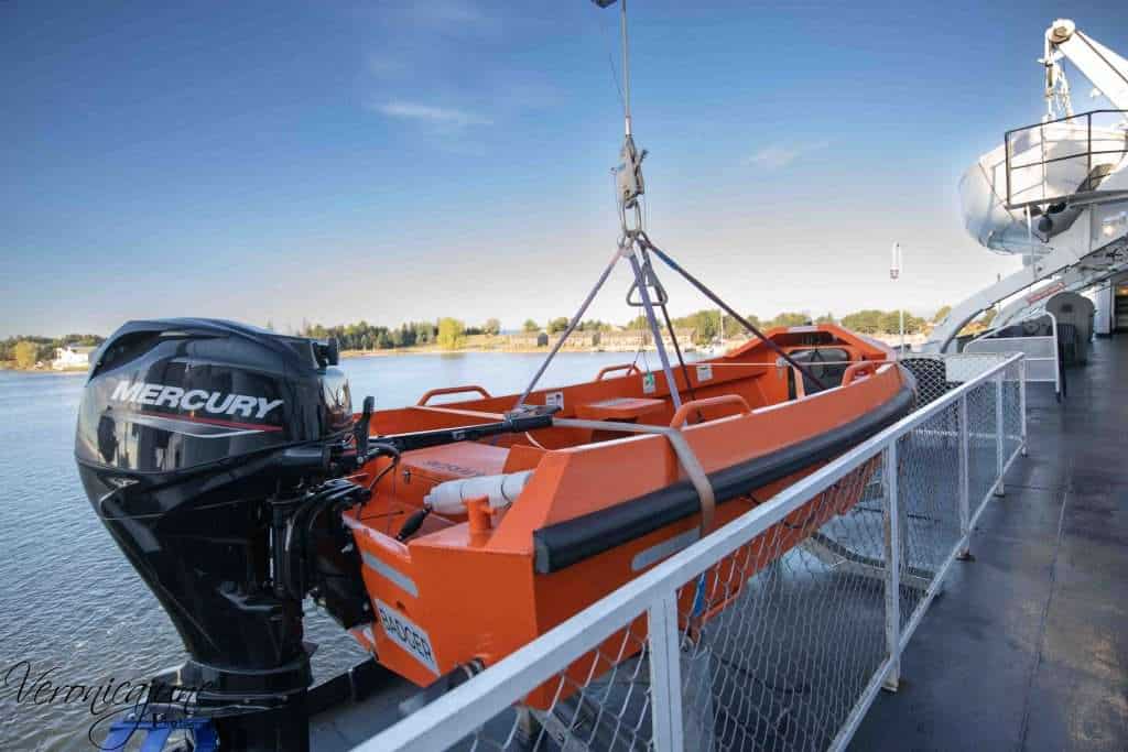 An orange lifeboat hangs off the side of the SS Badger with a blue sky and land behind