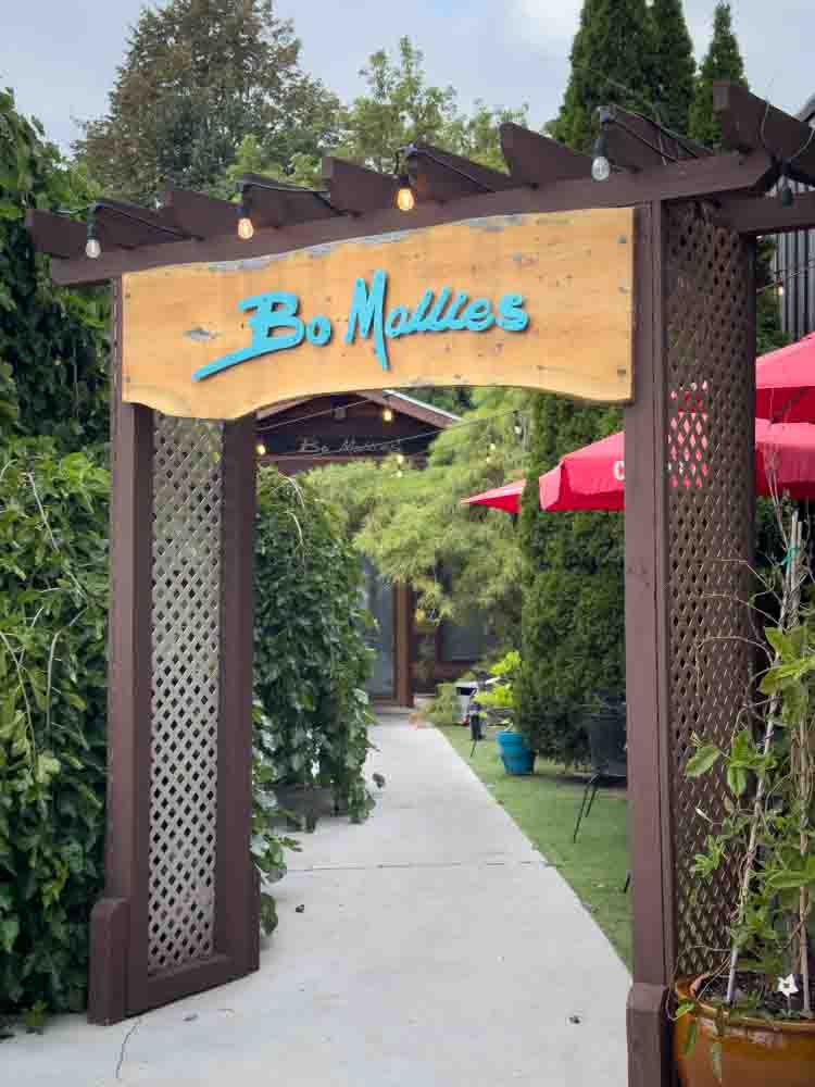 Bo Mallee restaurant entrance with wooden archway and garden outdoor seating, vibrant landscaping, and cozy ambiance - perfect for a relaxing dining experience.