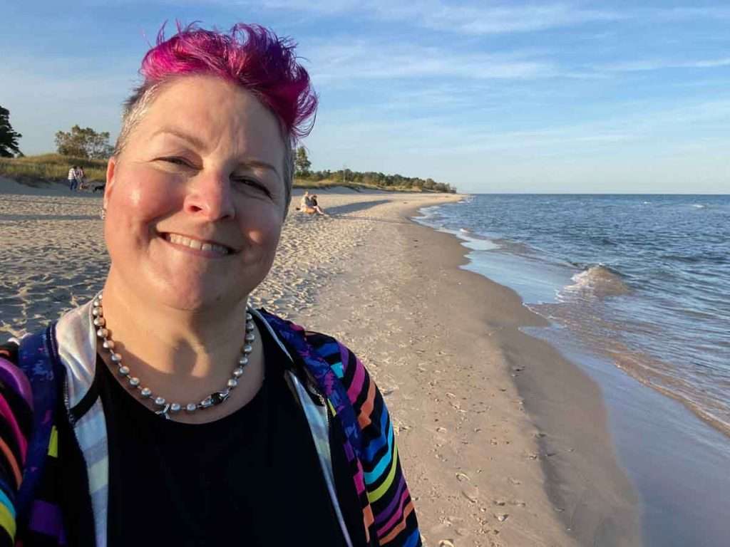 The author smiles with a beach stretching out behind her as far as the eye can see.
