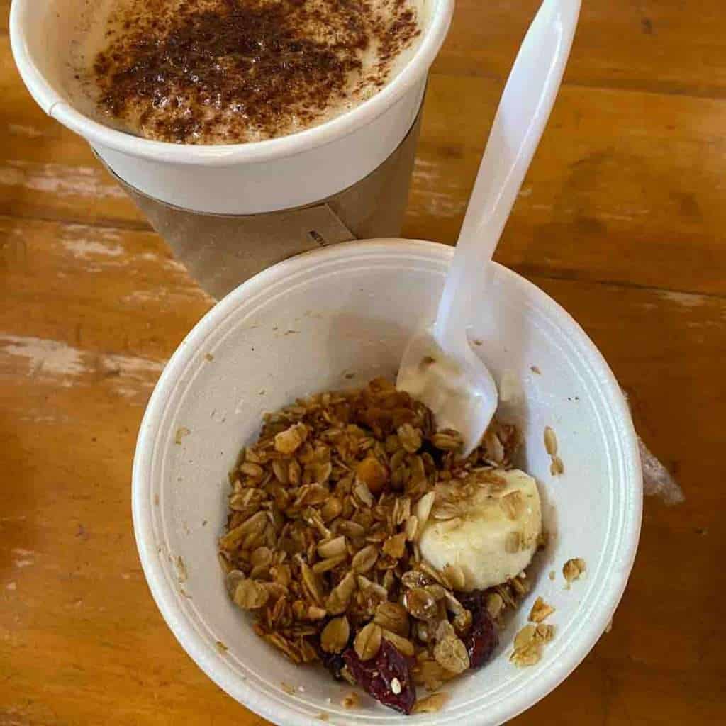 Creamy cappuccino with cinnamon topping and healthy granola yogurt parfait on wooden table.