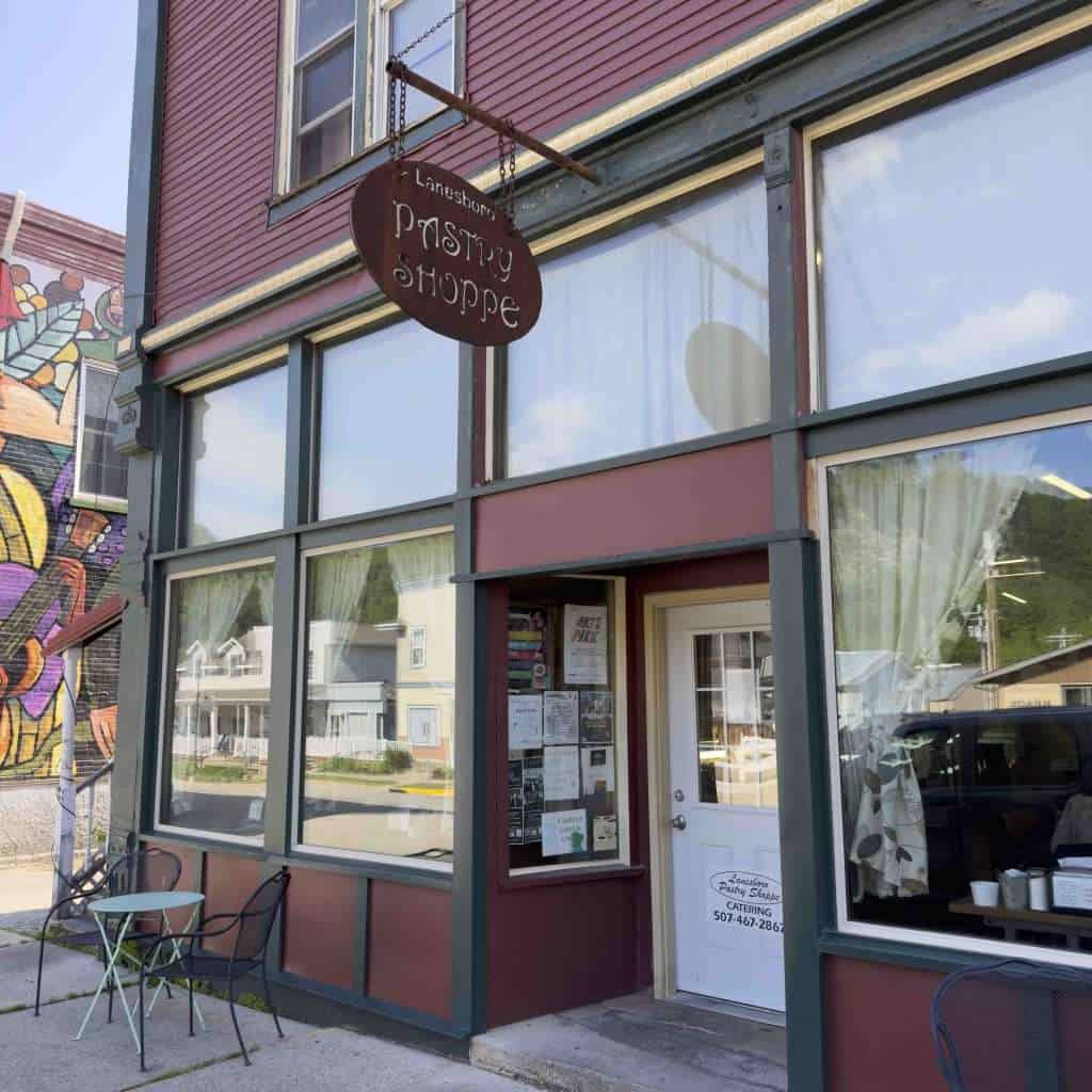 Handmade pastry shop exterior with vintage-style sign, colorful mural on the side, and cozy outdoor seating, perfect for enjoying baked goods and treats in a charming small-town setting.