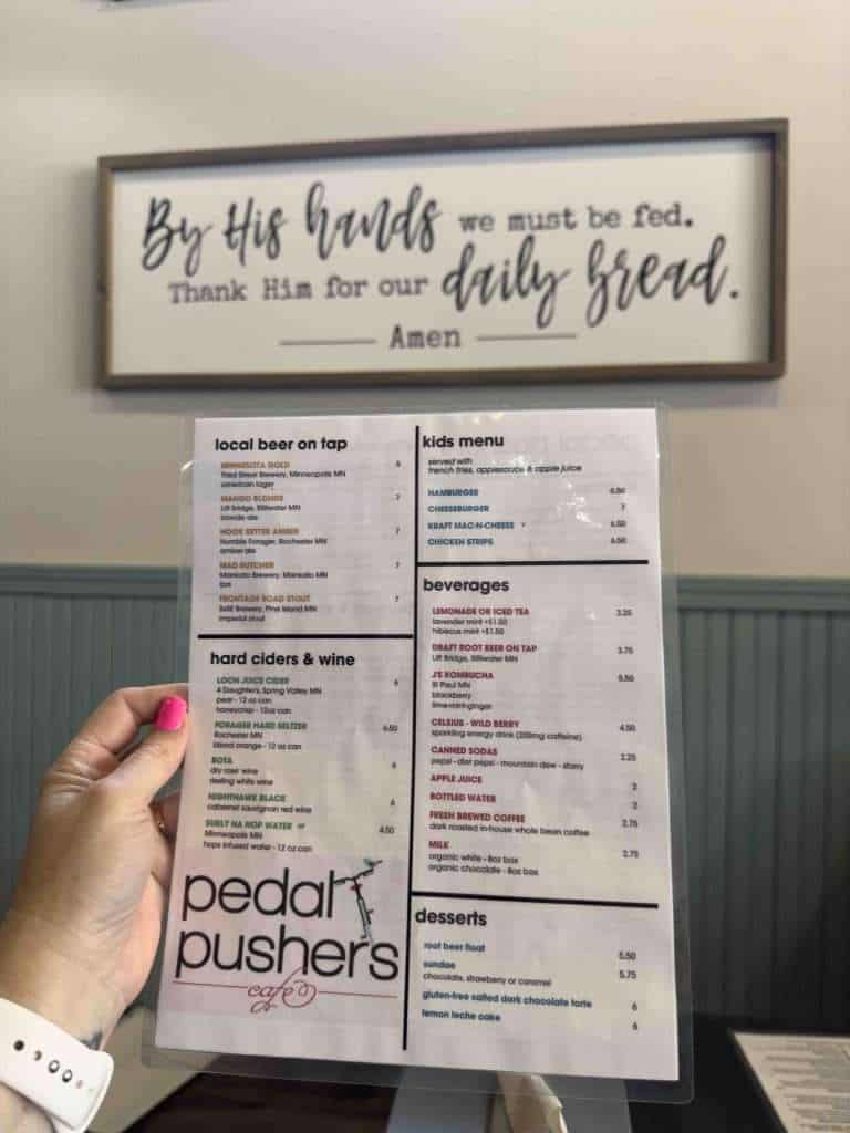 A Pedal Pushers Cafe menu in front of a sign with a positive message promoting a joyful, community-focused lifestyle